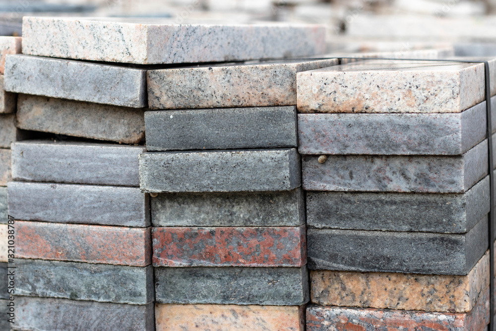 Pieces of white, grey, multicolored granite and marble. Cut into square slabs used for construction and decoration. Stacked in a warehouse for further use.