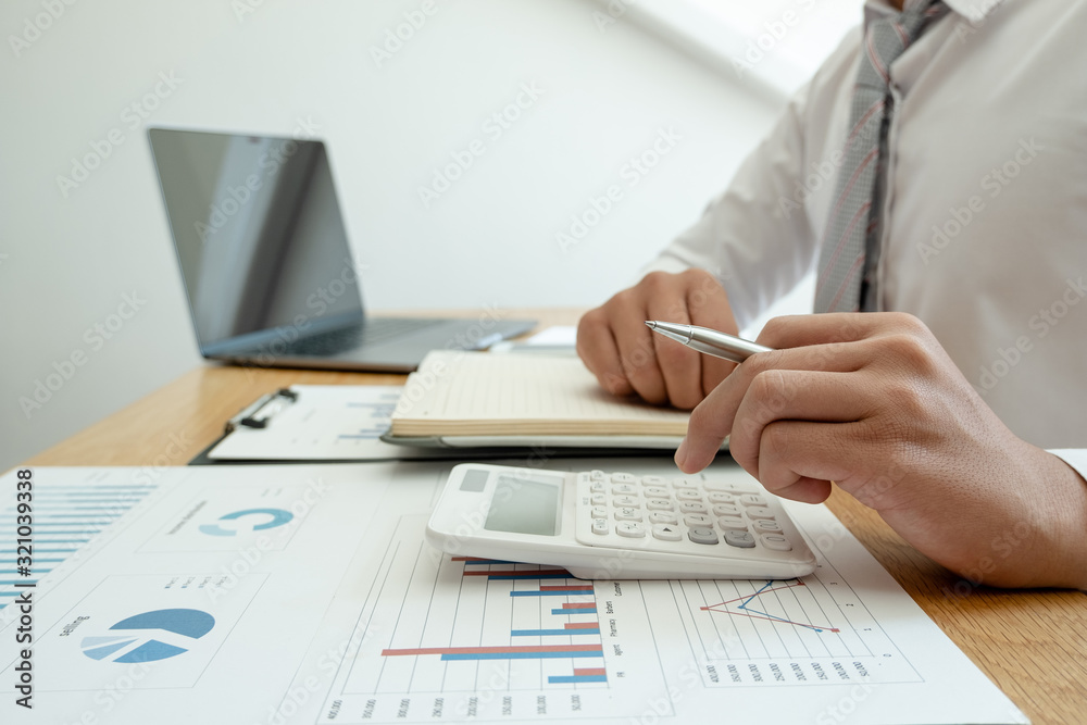A business man is sitting at a desk and calculating financial graphs about real estate investment expenditures A business man is sitting at a desk and calculating financial graphs about real estate investment expenditures