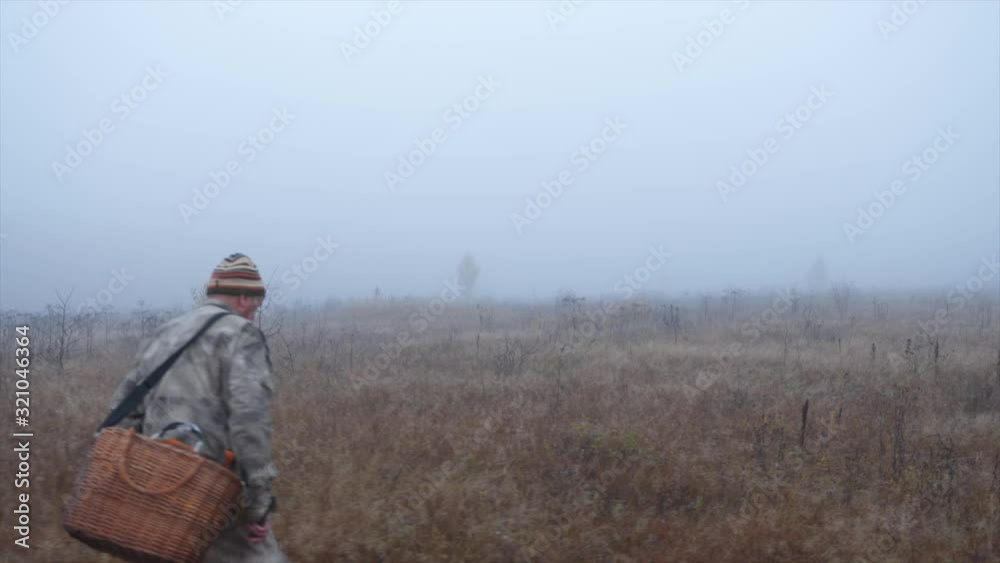 Gray army camouflage and walks along an empty field among weeds in the early morning in late autumn in wet weather in search of mushrooms Gray army camouflage and walks along an empty field among weeds in the early morning in late autumn in wet weather in search of mushrooms