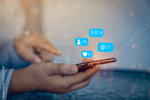 Person using a social media marketing concept on mobile phone with notification icons of like, message, comment above smartphone screen.