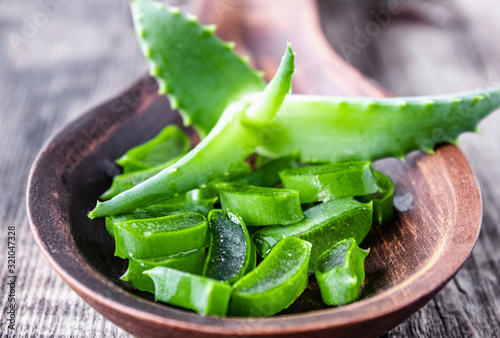 Green aloe leaves and slices of aloe vera in a spoon on a wooden background.