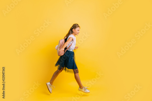 Happy little schoolgirl with a briefcase, rushing to school on an isolated yellow background