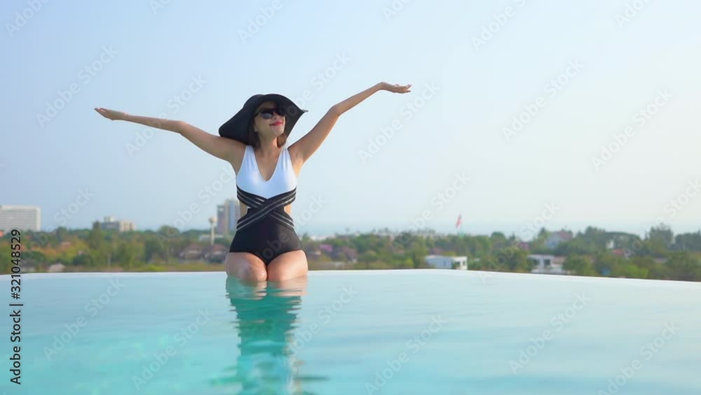 Still shot Happy Woman with hat and swimsuit relaxing on infinity pool edge Still shot Happy Woman with hat and swimsuit relaxing on infinity pool edge
