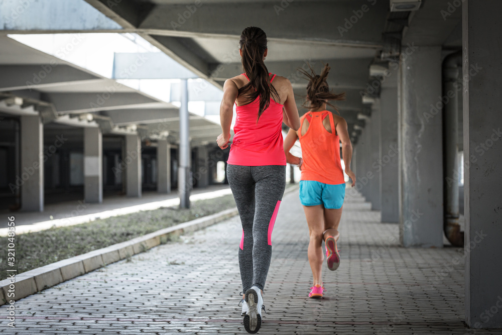 Two female runners jogging around the city road overpass.Urban workout concept.Rear view.