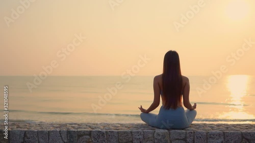 Young sports girl meditates at sunset, calm ocean sea, long hair photo