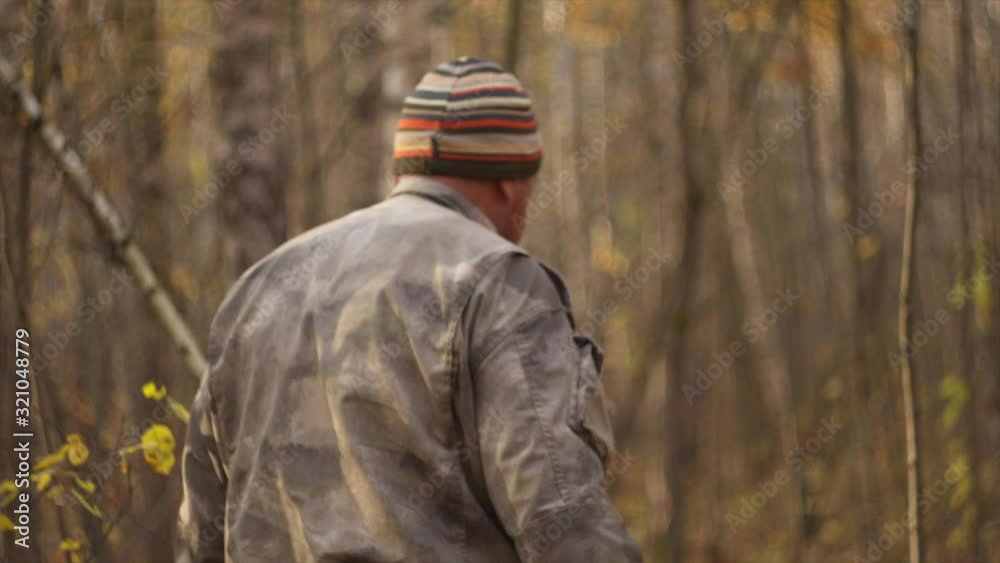 A man in gray camouflage, walks through the guest forest among birches, in late autumn, in the early morning, on raw yellow leaves, with a wicker basket on his shoulder and looking for mushrooms A man in gray camouflage, walks through the guest forest among birches, in late autumn, in the early morning, on raw yellow leaves, with a wicker basket on his shoulder and looking for mushrooms