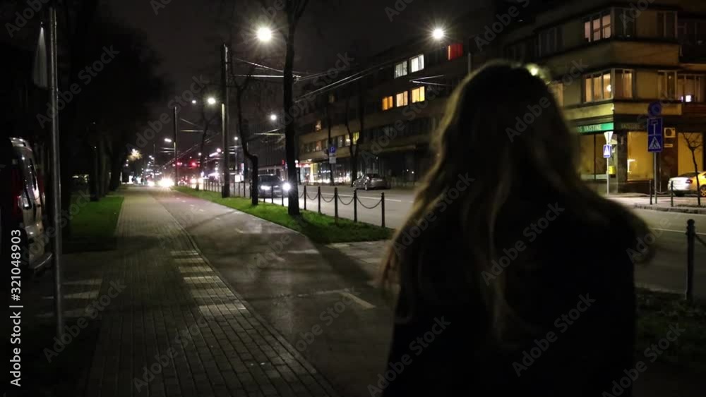 Girl taking a walk in the city at night time slow motion, view from the back