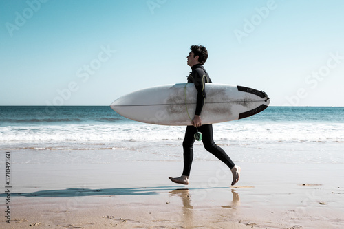 Photography Young man carrying surfboard and running on sunny beach
