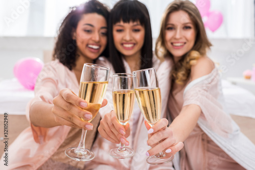 Photography selective focus of smiling multicultural girls clinking with glasses of champagn