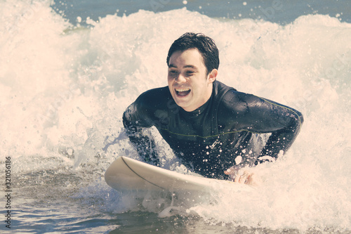 Excited young man swimming on surfboard in sea. Handsome guy wearing wetsuit and lying on board. Surfboarding and vacation concept. © Mangostar