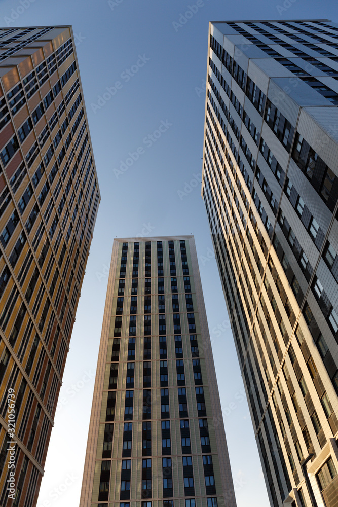Obraz premium bottom view: three modern residential towers in a modern residential complex in reflected sunlight against a blue sky