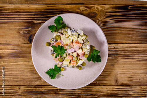 Ceramic plate with russian traditional new year salad olivier on a wooden table. Top view