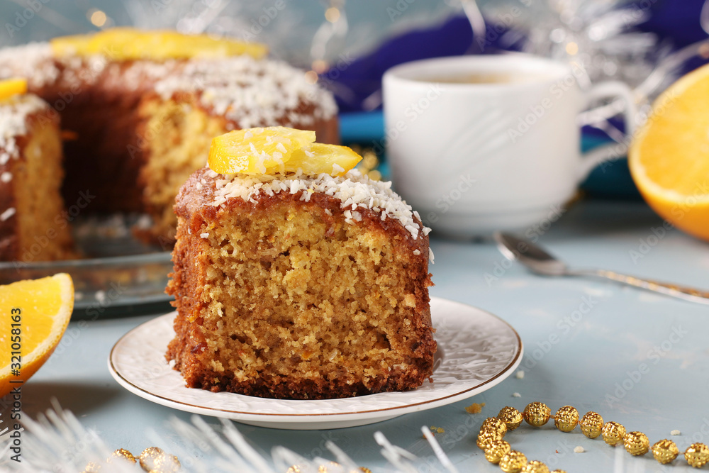 Homemade muffin with oranges sprinkled with coconut flakes on a light blue background and a cup of coffee, a piece of muffin in the foreground