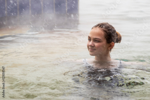 Girl in the pool with warm mineral water from a thermal spring in winter in snowy weather outdoors. Steam rises from warm water.