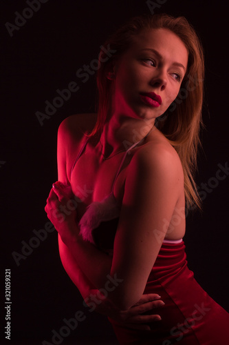 High Fashion model woman in colorful bright lights posing in studio, In a short red dress with white fur