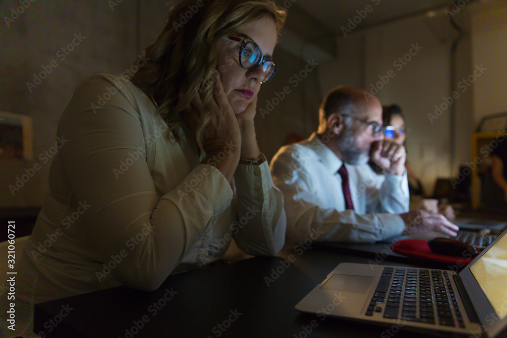 Focused business team working in dark office. Professional business people working with computers late at night. Working late concept