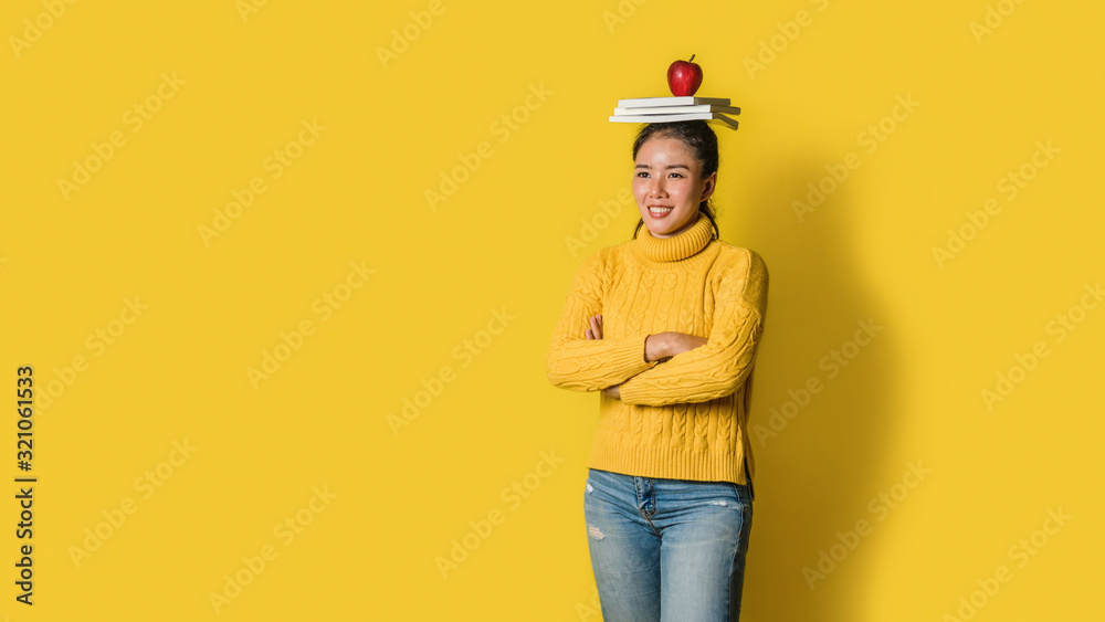 Cheerful young woman on yellow background in studio with a book and a red apple on her head. A smiling and happy girl. The concept of exercise for good health. Health lover Cheerful young woman on yellow background in studio with a book and a red apple on her head. A smiling and happy girl. The concept of exercise for good health. Health lover