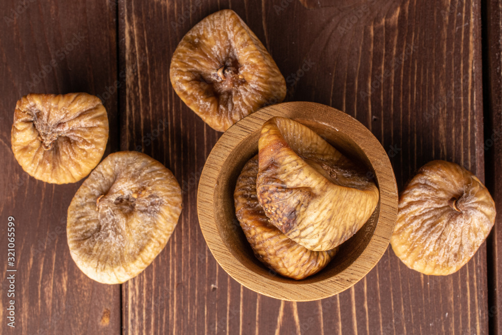 Group of six whole dried fig in bamboo bowl flatlay on brown wood