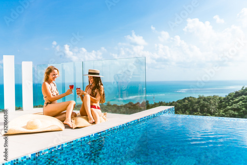 Beautiful girls having fun by the pool with wine and talking about travel and the weekend. Discuss March 8th. Holidays and parties by the pool in a villa by the sea. Thailand, Samui