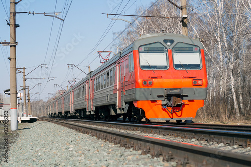 Bright beautiful Russian electric train of red, orange, gray. Railroad, posts with wires
