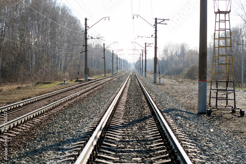 The railway goes into the distance. Rails, sleepers, poles with wires. Spring day