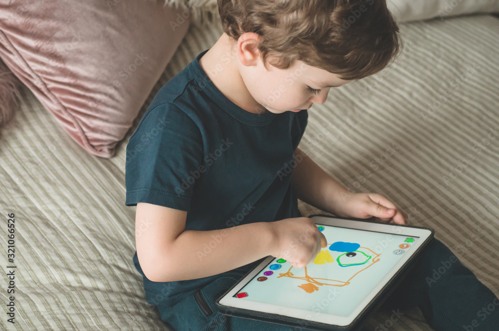 Boy sitting with a tablet in the room. The boy lies on a bed and plays on the tablet. Boy sitting with a tablet in the room. The boy lies on a bed and plays on the tablet.