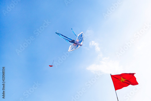 A kite flying against a clear, blue sky in Vietnam, the Vietnamese flag is developing nearby.