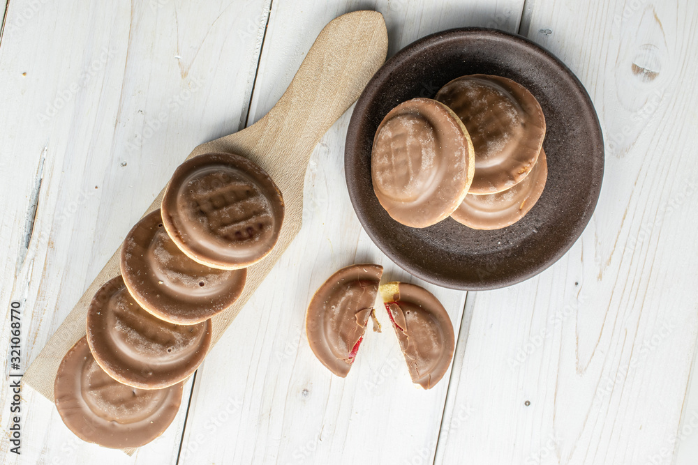 Group of seven whole two halves of chocolate biscuit with brown ceramic coaster on wooden cutting board flatlay on white wood Group of seven whole two halves of chocolate biscuit with brown ceramic coaster on wooden cutting board flatlay on white wood