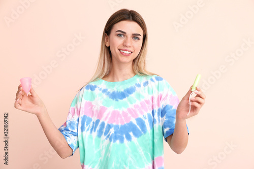 Young woman with menstrual cup and tampon on color background