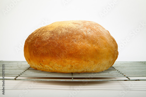 Freshly baked cob loaf of bread resting on a cooling rack isolated on a white background