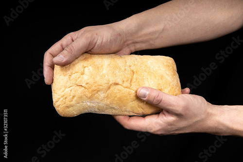 Fresh bread ciabatta in two male hands on black background