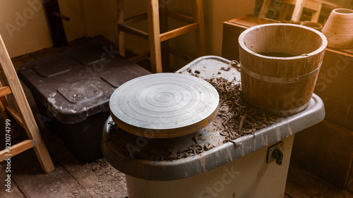 Pottery Wheel Machine for making hand crafted Ceramic such as bowls, plates and cups in foreground with wooden cask. Creative workshop.  photo