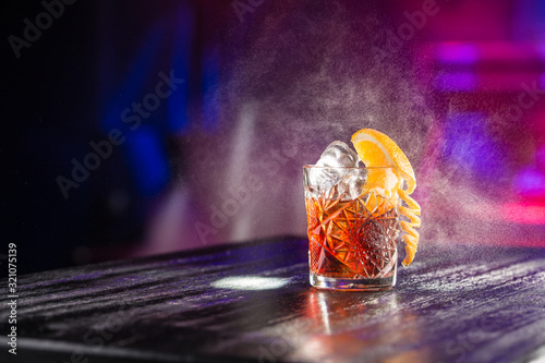 old fashioned classic cocktail in crystal glass with ice and orange on the table on nightclub background