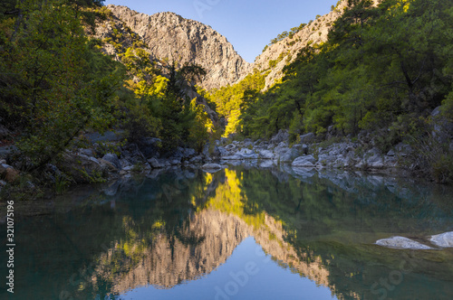 Beautiful green mountains of canyon reflected in mirror surface of rocky lake or river. Horizontal photography of peaceful scenic landscape of Turkey.