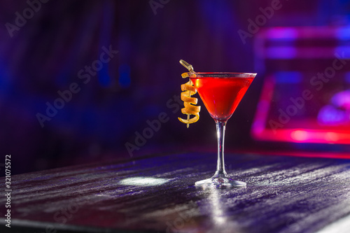 Red cosmopolitan cocktail with orange peel on the table on nightclub background