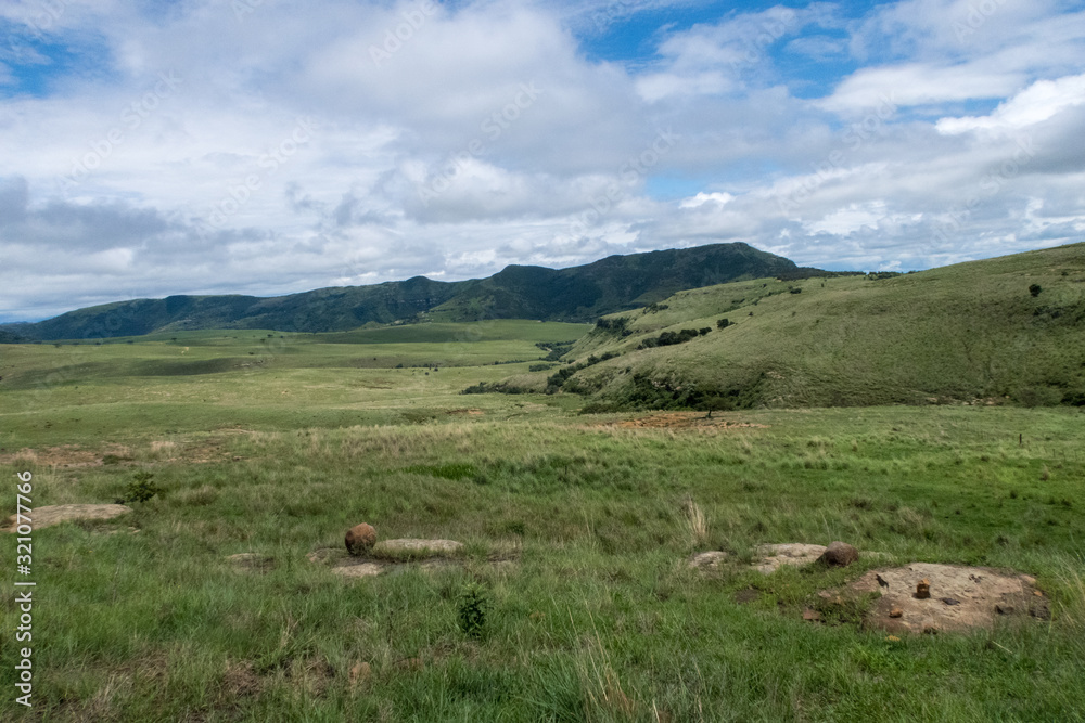 Wide open green fields with bright blue sky and white clouds in the Drakensberg Mountains in South Africa