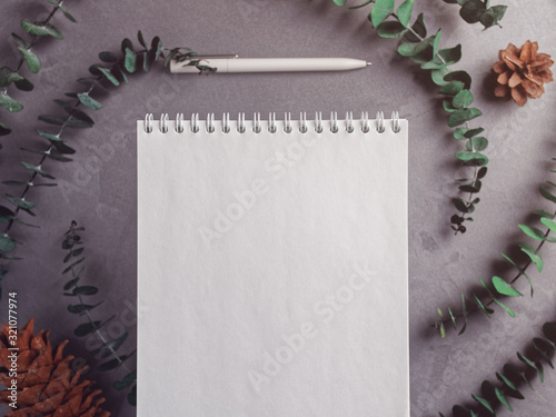 Notebook with flipcharts on a spring is on a gray background. Nearby are eucalyptus stems, cones and a pen. Flat lay. Copy space.