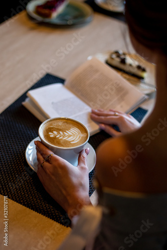 A Cup of coffee and an open book in a woman s hand