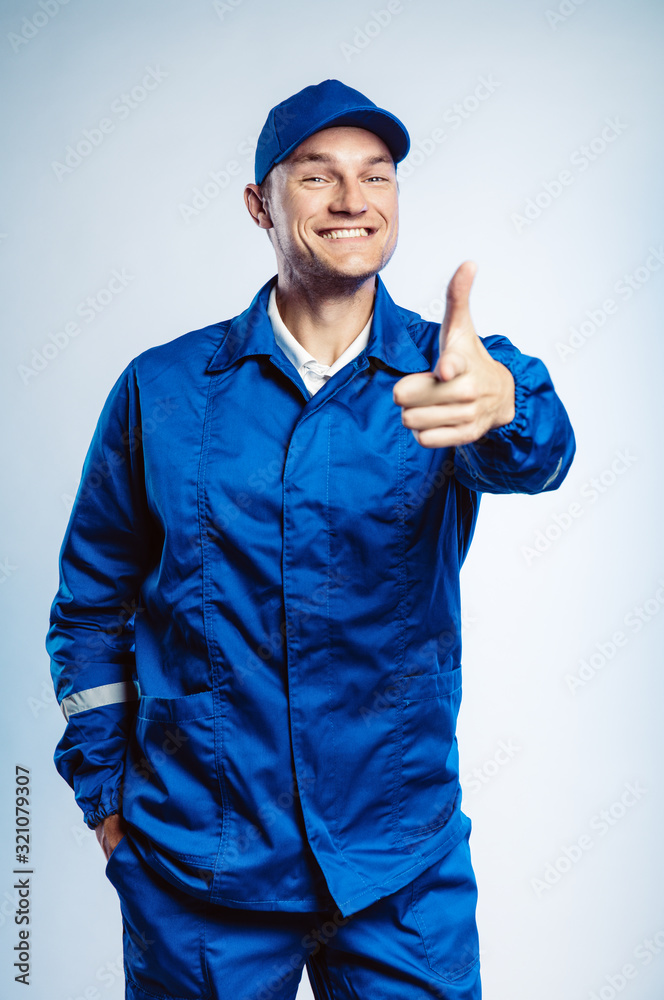 Portrait of young worker man wearing blue uniform. Pointing finger at you looking at camera. Isolated on grey background with copy space. Human face expression, emotion. Business concept.
