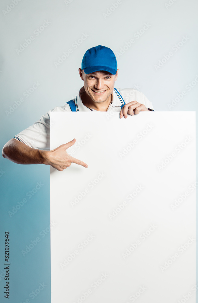 Mockup image of a young smiling worker holding empty white banner and points to it. Mockup image of a young smiling worker holding empty white banner and points to it.