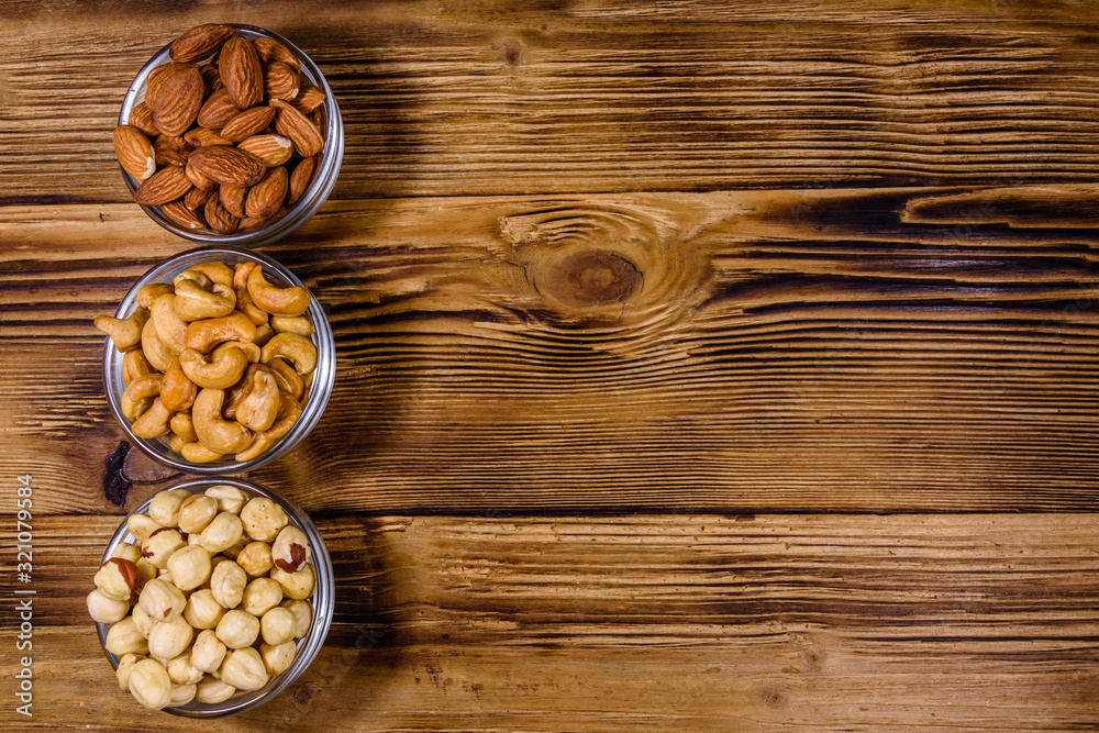 Various nuts (almond, cashew, hazelnut) in glass bowls on a wooden table. Vegetarian meal. Healthy eating concept. Top view Various nuts (almond, cashew, hazelnut) in glass bowls on a wooden table. Vegetarian meal. Healthy eating concept. Top view