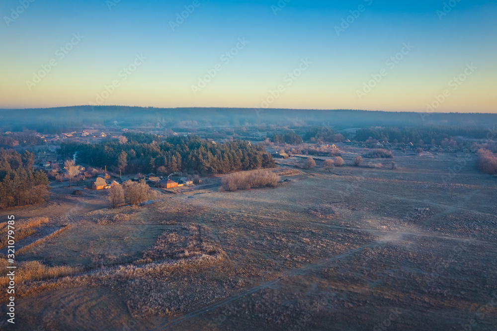 The surroundings of the Ukrainian village in the autumn clear weather. Aerial photo of village houses near the forest in a blue haze on the horizon.
