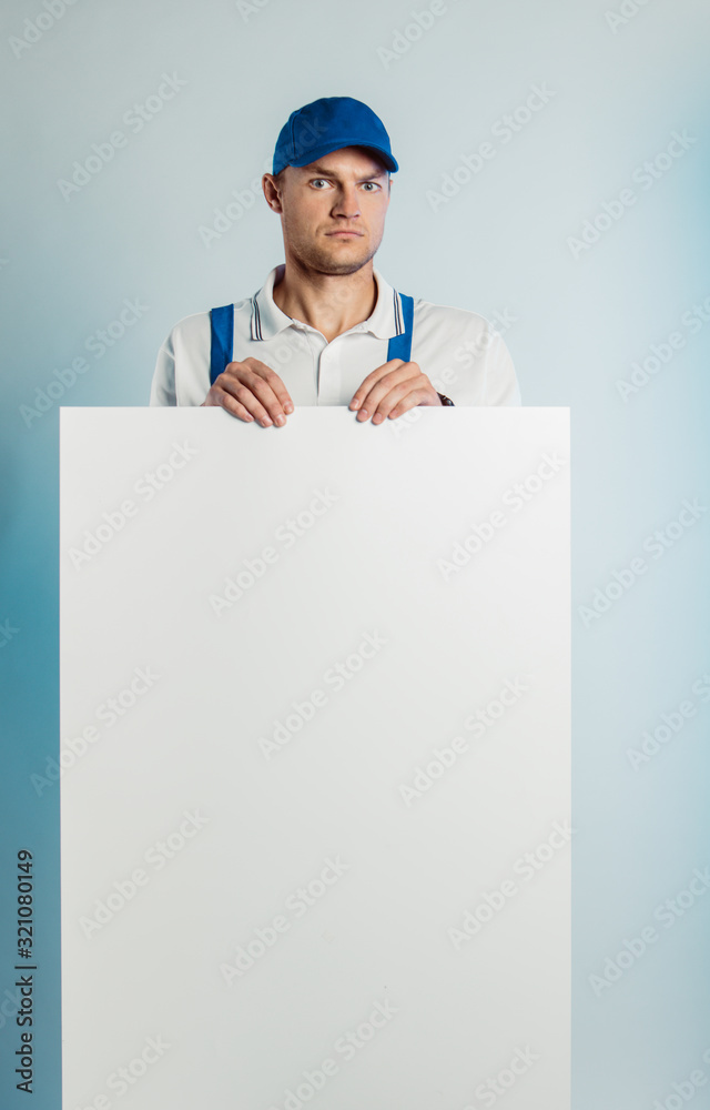 Mockup image of a young indignant worker holding empty white banner. White or blue background. Bussines concept. Mockup image of a young indignant worker holding empty white banner. White or blue background. Bussines concept.
