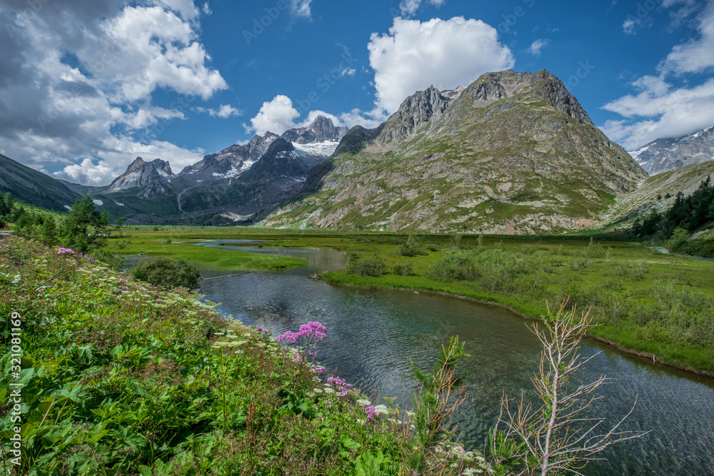 A beautiful alpine lake (Lac Combal) surrounded by lush green and pink foliage and high peaks