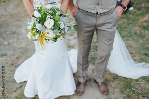 The groom in a gray suit and the bride in a white dress are holding a large bouquet of flowers close-up: chrysanthemums, roses, wildflowers. Photography, concept.
