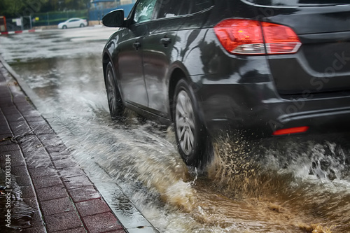 A car at high speed drives through a large puddle, Rain splash, raindrops and circles on the water. Israel, Rain, Flooding on the road