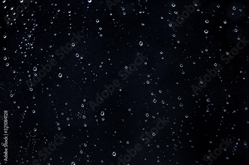 Rain water drops on a black dramatic window glass. Autumn depression background. Rain pattern.
