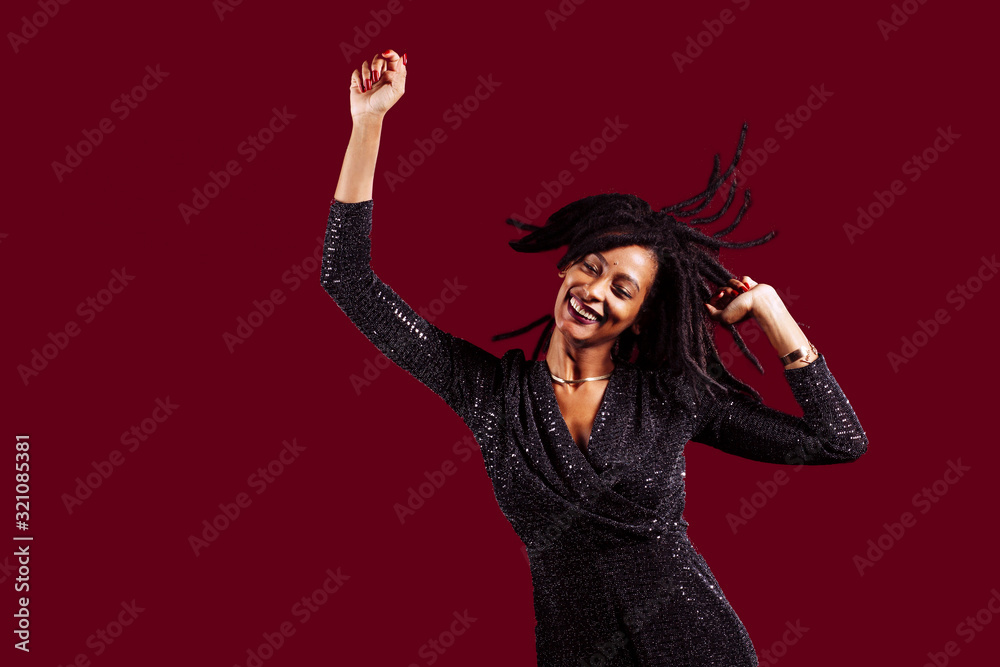 Portrait of a smiling woman with dreadlocks wearing a sparkly dress dancing with arms up celebrating, happy, fun