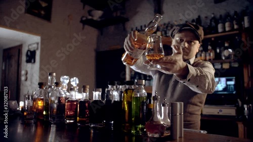 The bartender pours whiskey into a tasting glass (glencairn).  A bar counter in the speakeasy style. Dark scene, slow motion, camera movement.