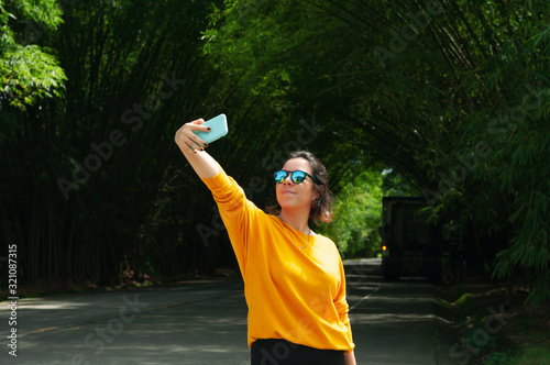 woman in yellow sweater and sunglasses, taking a selfie during a stop on the bamboo road, during spring, open view